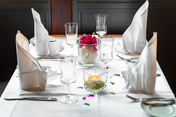 Table setting in a restaurant. Glass goblets, plates, candle, white napkins and decor on a white tablecloth