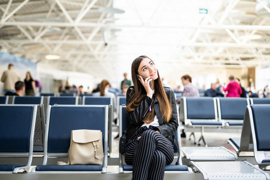 Air travel concept. Young casual woman on smart phone at gate waiting in terminal sitting with hand luggage