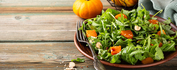 Salad diet paleo dengan arugula, labu panggang, kemiri dan biji wijen di atas piring cokelat. Konsep makanan sehat dengan ruang fotokopi. Spanduk.