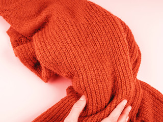 Cozy orange sweater on pink with woman's hand holding it