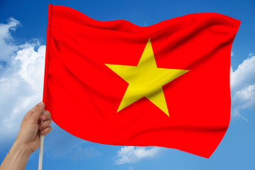 hand holds against the background of the sky with clouds the colored flag of Vietnam on the texture of the fabric, silk with waves, close-up
