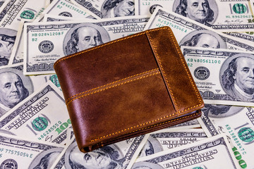 Closed brown leather wallet on the one hundred dollar banknotes