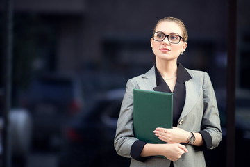 business woman in glasses and a suit holds a folder in her hands. Woman on the street waiting for a meeting