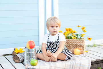 Portrait of  little blond boy sitting on a wooden porch at home on an autumn day. Childhood concept. The baby is happy. Little farmer. Healthy family lifestyle. Harvest time in the fall. Little farmer