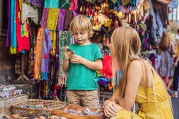 Mom and son travelers choose souvenirs in the market at Ubud in Bali, Indonesia