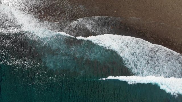 Aerial drone bird's eye view downwards shot of the waves hitting the sandy beach in Mamanuca, Fiji