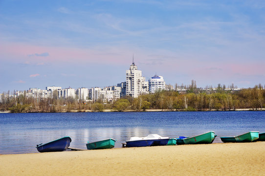 'Alye Parusa' Park (Red Sails) in Voronezh, Russian Federation. City view from sand beach and line of small green boats on reservoir waters and white tower.