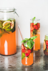 Homemade fresh strawberry and basil lemonade or ice tea in glass tumblers with eco-friendly plastic-free straws on grey concrete table, white wall at background. Cold refreshing soft drink