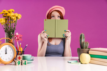 Image of caucasian student girl covering her face with diary book while sitting at desk
