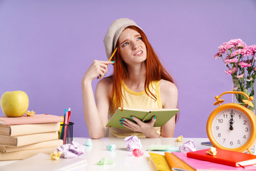Photo of confused student girl writing in exercise book while doing homework