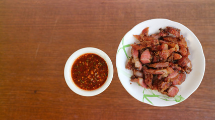 Grilled pork with dipping sauce on a white plate, brown wood background