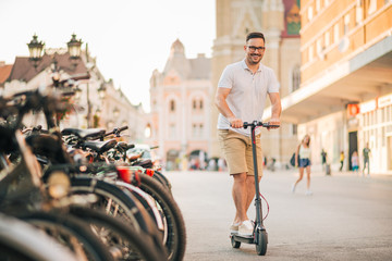 Smiling man riding electric scooter in european town on a sunny day, portrait. © bnenin