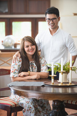 Asian male and female couples who wear white shirts and women wear floral dresses while smiling and sitting at the kitchen table.