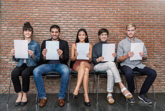 Portrait of happy young asian caucasian business people waiting for job interview hands holding white paper. Group Of People Sitting On Chair In A Waiting Room. Competitive lifestyle concept