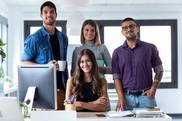 Successful business team posing grouped around an attractive young woman looking at the camera in the coworking space.
