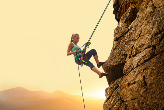 Beautiful Woman Climbing on the Rock at Foggy Sunset in the Mountains. Adventure and Extreme Sport Concept