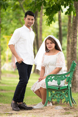 Portrait of young Asian couple in park. Woman wearing a white dress with a man wearing a white shirt, black pants and leather shoes.