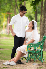 Portrait of young Asian couple in park. Woman wearing a white dress with a man wearing a white shirt, black pants and leather shoes.