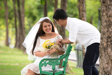 Portrait of young Asian couple smiling in park. Woman wearing a white dress with a man wearing a white shirt, black pants and leather shoes.