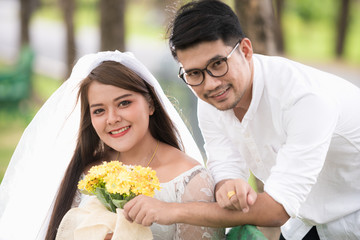 Portrait of young Asian wedding couple smiling and holding flowers in park.