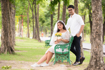Portrait of young Asian wedding couple smiling and holding flowers in park.