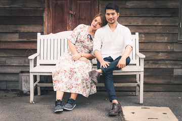 Attractive asian couple smiling and sitting on wooden chair.