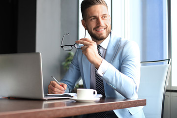 Portrait of happy businessman sitting at office desk, looking at camera, smiling