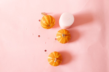 Halloween composition of pink candles, small pumpkins and glitter decor over pink background. Seasonal autumn background