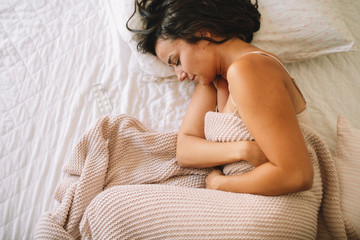 Young woman having stomachache lying on white bed