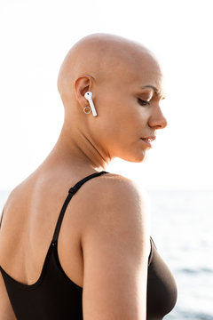 Image closeup young bald woman using earphone and looking downward