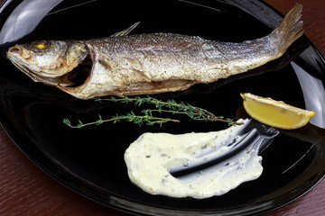 baked sea bass with sauce and lemon in a plate