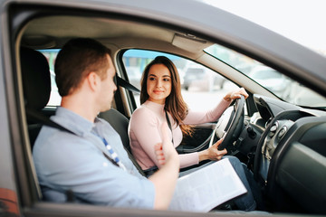 Male auto instructor takes exam in young woman. Positive happy model look at guy and smile. Driving car alone and careful. Guy talks to her. Passing exam.