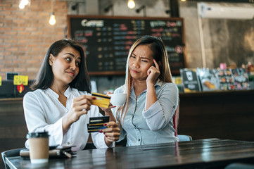 Two women sitting talking about a credit card in a coffee shop and having stress