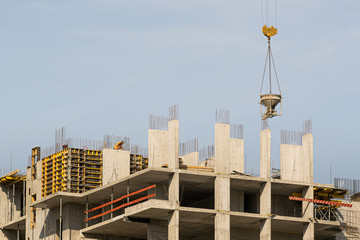 Fototapeta na wymiar A high-rise construction crane against the blue sky builds multi-storey residential buildings using modern technologies of metal, concrete and brick according to the architectural design