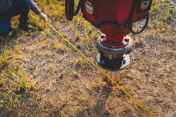 technician installing ground screw for mounting structure of solar panel at solar farm