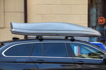 Modern car with luggage box on the roof parked on the side of city street.