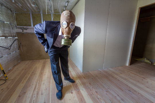 Strange man in businessman suit and gas protection mask inside a room under renovation works.