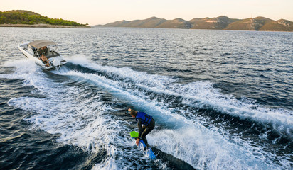 Aerial photo of man practicing wakeboarding towed by speed boat in deep blue sea