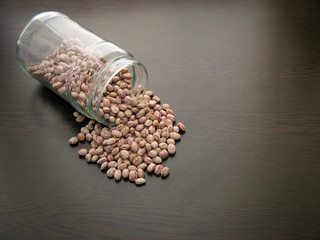 Pinto bean seeds glass jar. Pinto bean seeds are poured from a glass jar on brown wooden surface....