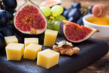 Cheese cubes, fresh fruit figs grapes Honey walnut on wooden chopping Board. Selective focus. Close up.