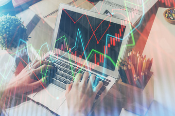 Double exposure of man's hands writing notes of stock market with forex graph background. Concept of research and trading.