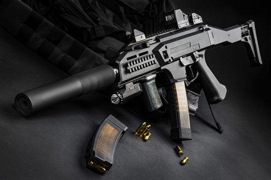 Modern automatic rifle with a silencer and a collimator sight on a dark background. Tactical submachine gun. Weapons for the police and special units. Studio shot.