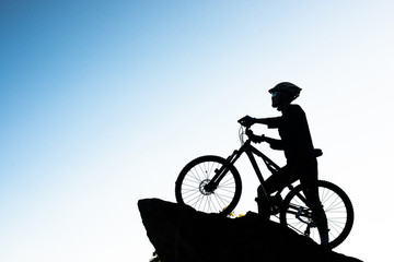 Fototapeta na wymiar Silhouette of the athlete standing on the rock with bicycle