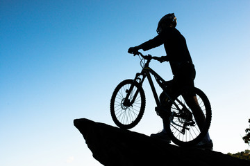 Silhouette of the athlete standing on the rock with bicycle