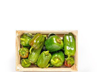 Green peppers and zucchini are in a wooden box on a white background.