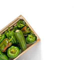 Green peppers and zucchini are in a wooden box on a white background.