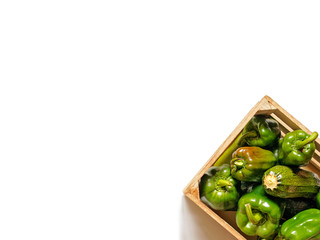 Green peppers and zucchini are in a wooden box on a white background.