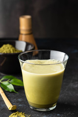 Matcha green tea latte in glass mug with whisk.