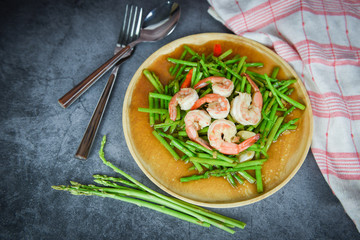 Fried asparagus shrimp prawns cooking food on wooden plate and fresh asparagus bunch on the dining table