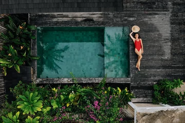Tafelkleed Luchtfoto drone foto van gelukkige vrouw in rode zwembroek ontspannen in de buurt van privé zwembad met bloemen en groen rond, Bali. Tropische achtergrond en reisconcept. © tatyanasuyarova